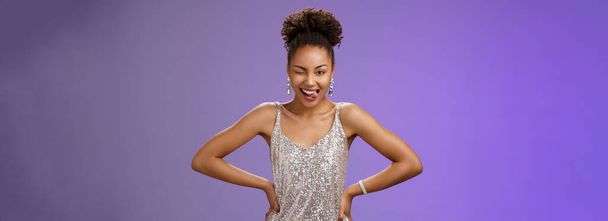 Pimasz jóképű afro-amerikai nő ezüst csillogó ruha fogd meg a kezét derék show nyelv merész kacsintó kamera úgy érzi, szerencsés áll izgatott tánc szórakozás bulizás, kék háttér. - Fotó, kép
