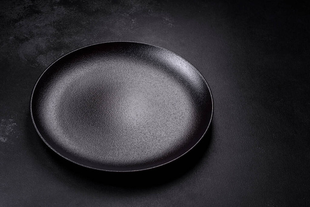 Empty black ceramic plate on a dark concrete background. Preparing the table for a family dinner - Foto, imagen