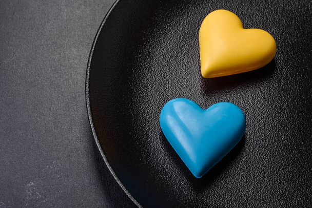 Шоколадные сердечки в цветах украинского флага на черной керамической пластине. День святого Валентина в украинских цветах - Фото, изображение