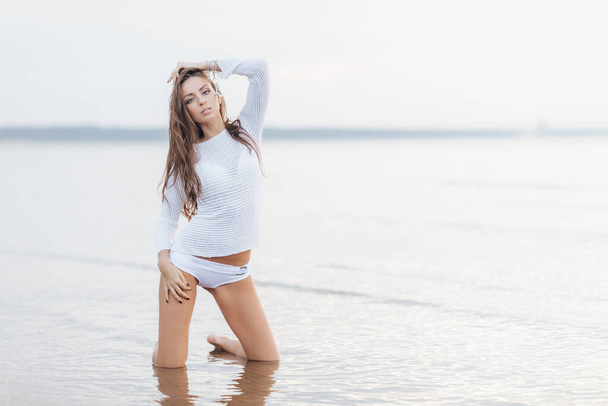 Atractivas modelos femeninas jóvenes en la costa contra la hermosa vista al mar y el cielo despejado, lleva bikini, se pone de rodillas, disfruta de la maravillosa naturaleza y la soledad. Forma y forma corporal perfectas
 - Foto, Imagen