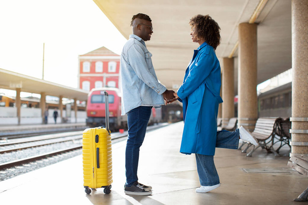 Tren istasyonunda durup el ele tutuşan, genç Afrikalı Amerikalı erkek ve kadınları seven romantik siyah çift tren gelene kadar hassas anlar yaşıyor. - Fotoğraf, Görsel