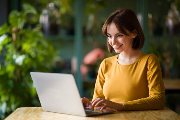 Concentrated at work, women in business. Confident cheerful young brunette woman in smart casual wear working on modern laptop while sitting at table in creative office or cafe, copy space - Photo, Image
