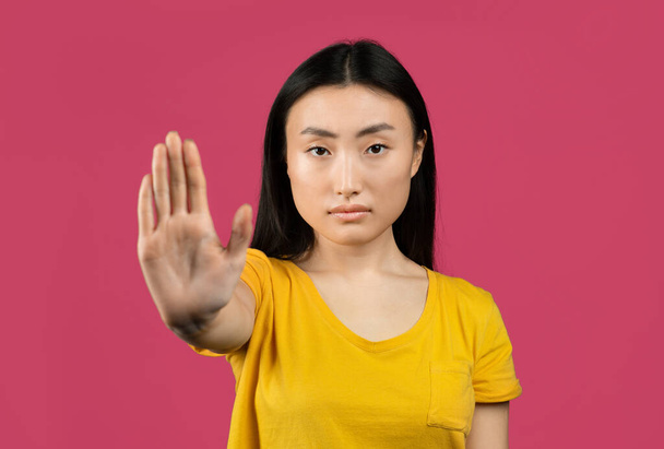 Jonge Japanse dame gebaren STOP, zeggen NEE, tonen afwijzing gebaar, uiten van haar negatieve houding, poseren op roze studio achtergrond - Foto, afbeelding