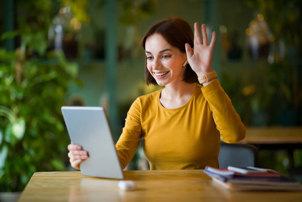 Portret atrakcyjnej młodej kobiety siedzącej w kawiarni podczas rozmowy wideo ze swoimi partnerami biznesowymi, młoda uśmiechnięta kobieta dzwoniąca przez łącze internetowe na tablecie dotykowym, przestrzeń do kopiowania - Zdjęcie, obraz