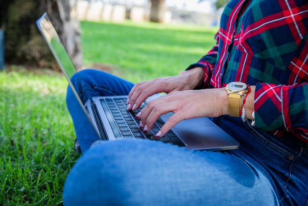 Close-up van de handen van een meisje typen op haar laptop zittend in een openbaar park - Foto, afbeelding