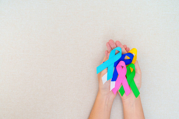 Всесвітній день раку, 4 лютого. Рука тримає сині, червоні, зелені, білі, рожеві, військово-морські сині та жовті стрічки для підтримки людей, що живуть та хворіють. Концепція Дня здоров'я та аутизму
 - Фото, зображення