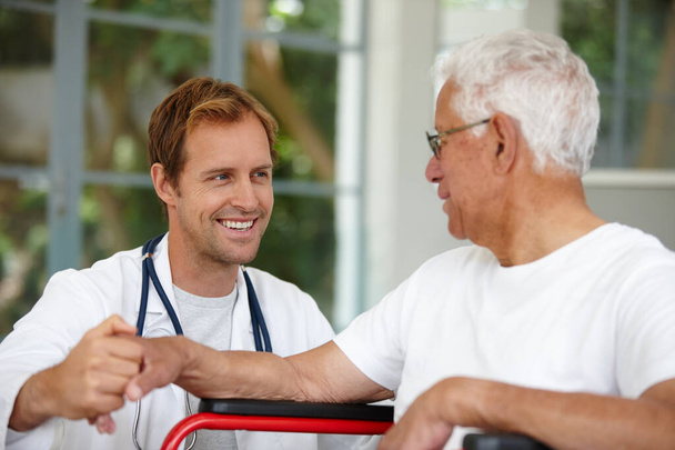 Είναι υποστηρικτικός επαγγελματίας υγείας. Ένας όμορφος άντρας γιατρός μιλάει με τον ασθενή του που είναι σε αναπηρική καρέκλα. - Φωτογραφία, εικόνα