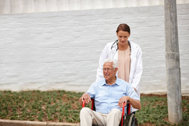 Mit ihrer Patientin auf Spritztour. Ärztin schiebt ihre ältere Patientin im Rollstuhl nach draußen - Foto, Bild