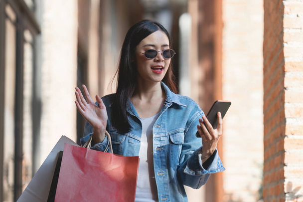 Asiatische modische Frau spaziert mit Einkaufstüten durch Einkaufszentrum, während Flash Sale Promotion läuft. - Foto, Bild