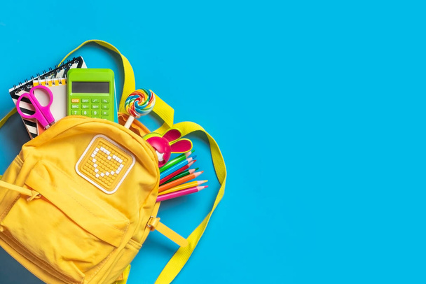 Retour à l'école, concept éducatif Sac à dos jaune avec fournitures scolaires - bloc-notes, stylos, gomme arc-en-ciel, numéros isolés sur fond bleu. - Photo, image