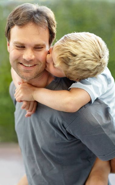 Egy fiú szeretete. Fiatal fiú csókolja apja arcát, miközben ő ad neki egy piggyback - Fotó, kép