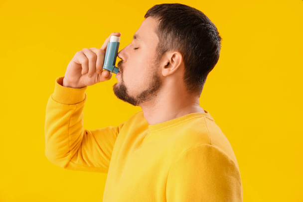 Sick man with inhaler on yellow background - Foto, imagen