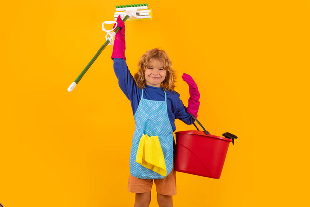 Τα παιδιά βοηθούν στο νοικοκυριό, καθαρίζουν το σπίτι. Υπηρεσία καθαριότητας στο σπίτι. Χαριτωμένο παιδί αγόρι βοηθά με την καθαριότητα στο κίτρινο στούντιο backdround - Φωτογραφία, εικόνα
