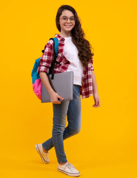 Schulkind, jugendliches Studentenmädchen mit Laptop auf gelbem isolierten Studiohintergrund. Kinderschul- und Bildungskonzept. Glücklicher Teenager, positive und lächelnde Gefühle eines Teenie-Mädchens - Foto, Bild