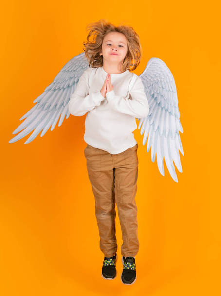 小さな天使のジャンプ、子供たちのジャンプ、全身。バレンタインデー。黄色のスタジオの背景に天使の翼を持つブロンドのかわいい子供。幸せな天使の子 - 写真・画像
