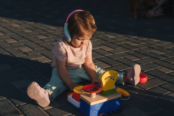 Malá holčička sedí na podlaze na dvorku a hraje si o letních víkendech se vzdělávací hračkou. Bavíte se s barevnými bloky - Fotografie, Obrázek