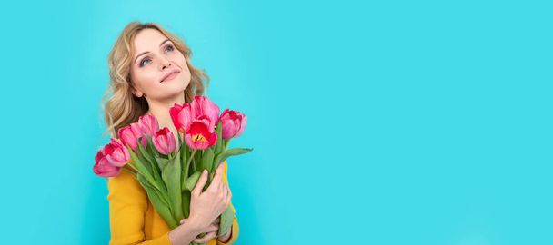 verträumte, glückliche junge Frau mit frühlingshaften Tulpenblüten auf blauem Hintergrund. Frau isoliert Gesicht Porträt, Banner mit Attrappe Kopierraum - Foto, Bild