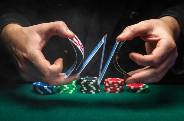Опытный дилер или крупье тасует карты в клубе над зеленым столом с игральными фишками. Концепция игры в покер в казино или клубе. - Фото, изображение