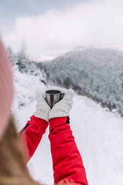 Traveler woman holding cup of coffee on the background of the mountains. Adventure, travel, winter concept. - Photo, Image