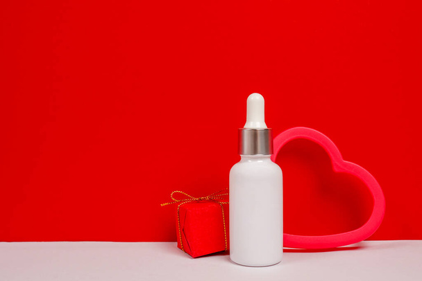 Kırmızı arka planda kalp ve hediye kutusu olan kozmetik yağ şişesi. - Fotoğraf, Görsel