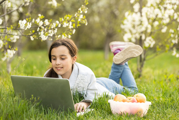 Tyttö, joka käyttää kannettavaa tietokonetta takapihalla. Lapsi opiskelee kotona tekemässä kotitehtäviään tai ottaa online-oppitunnin. Kotikoulun käsite - Valokuva, kuva
