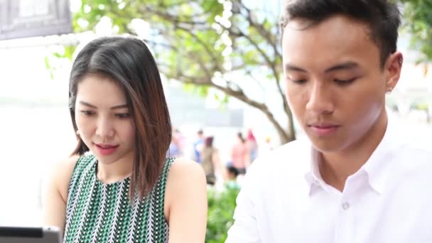 Asiático casal ao ar livre sentado em uma mesa de restaurante usando tablet. - Filmagem, Vídeo