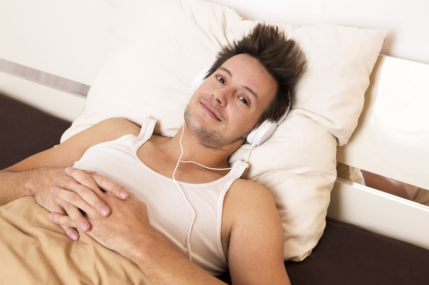 Умный парень лежит в постели и слушает музыку.
 - Фото, изображение