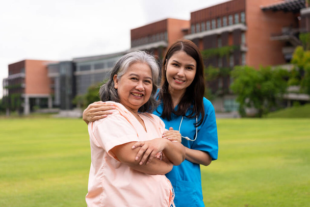 Азиатский заботливый ухаживающий или медсестра держат пациента за руку и поощряют пациента в саду. Концепция счастливого выхода на пенсию с заботой от сиделки и сбережений и медицинского страхования для пожилых людей. - Фото, изображение