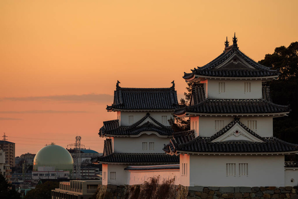 Sunset light hits historic Japanese castle near spherical liquid storage tank. High quality photo - Photo, Image