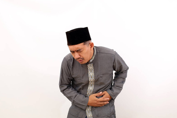 Azjatycki muzułmanin cierpiący na ból lewego brzucha. Izolacja na białym tle - Zdjęcie, obraz