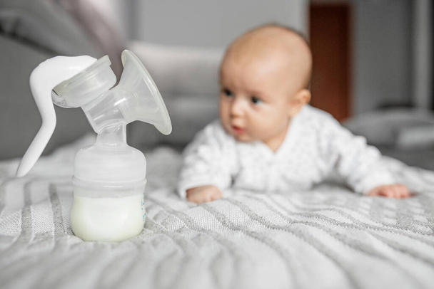 Child care concept. Breast pump with milk on background of small cute baby. Selective focus, copy space. - Photo, image
