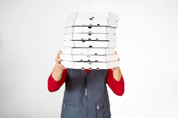 Kuva onnellisesta toimittajasta punaisessa t-paidassa ja korkissa, joka antaa ruokatilauksen ja pitää monia pizzalaatikoita eristyksissä valkoisella taustalla - Valokuva, kuva
