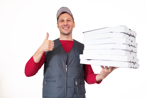 Photo of happy delivery man in red t-shirt and cap giving food order and holding many pizza boxes isolated on white background - Foto, imagen