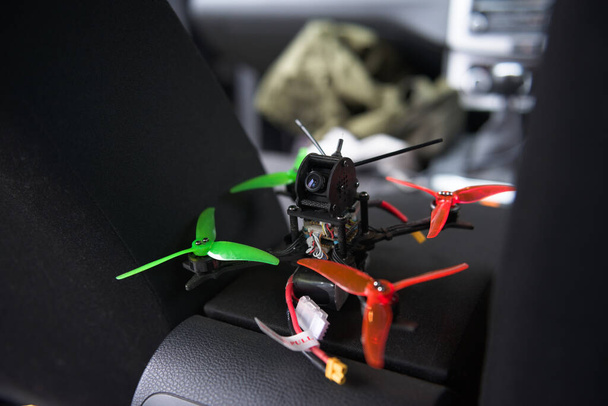 Close up selective focus image of small drone resting on a car armrest. Selective focus, with the remote first person view camera clearly visible. - Foto, Imagen