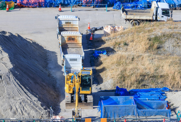 Earth mover and flatbed trucks parked by sand piles at empty construction site on sunny day. High quality photo - Photo, image