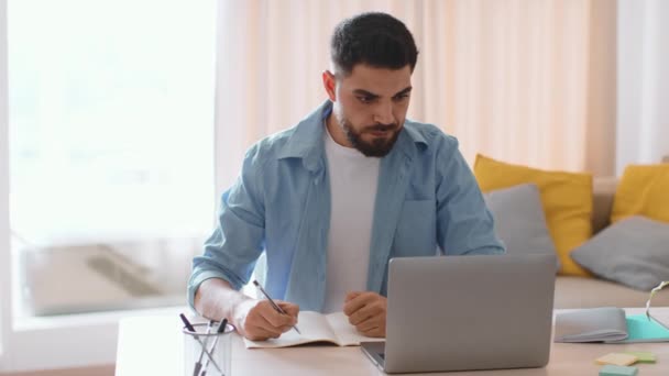 E-learning concept. Young focused middle eastern man student studying online at home, watching webinar and writing notes, tracking shot, slow motion, free space - Filmagem, Vídeo