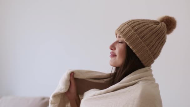 Πρόβλημα θέρμανσης διαμερίσματος. Πορτραίτο προφίλ παγωμένης νεαρής γυναίκας που φοράει πλεκτό καπέλο σκεπασμένη με ζεστή κουβέρτα, ατενίζοντας κενό χώρο, αργή κίνηση - Πλάνα, βίντεο