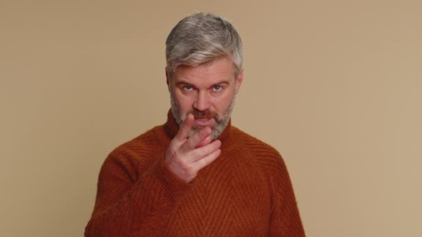 I am watching you. Caucasian man in sweater pointing at his eyes and camera, show I am watching you gesture, spying on someone. Senior adult middle-aged guy isolated alone on beige studio background - Séquence, vidéo