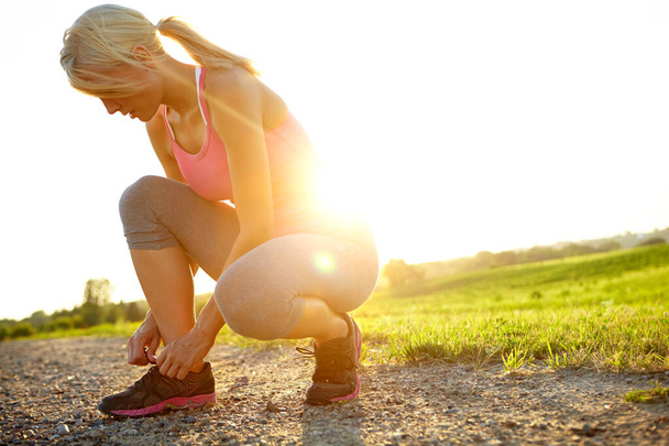 Zieht ihre Laufschuhe an. Eine junge Frau in Sportbekleidung bindet ihre Schnürsenkel - Foto, Bild