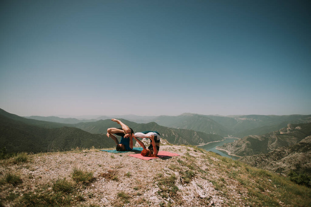 Yoga couple doing some yoga poses with legs up at the top of the mountain - Photo, Image