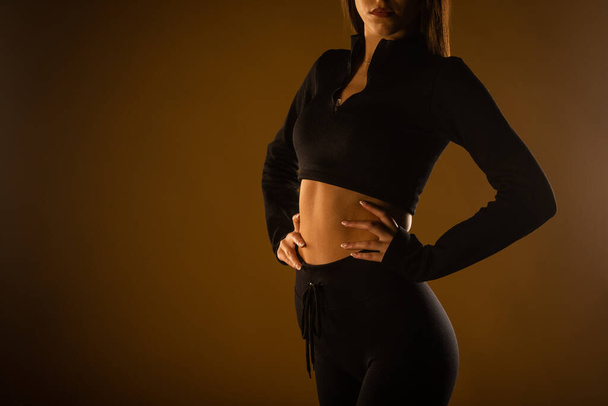 Girl with hands on her spine posing in black sports bra and black leggings. Close up photo - Photo, image