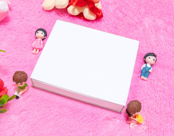 White blank rectangle box above a fluffy pink carpet surrounded by dolls - Foto, imagen