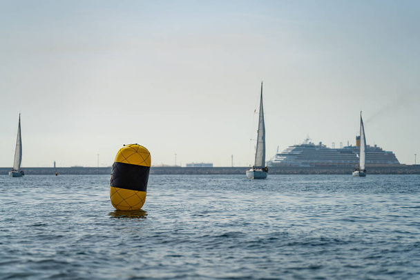 Yellow buoy with blurred sailing ships and passenger ferry in the background - Foto, imagen