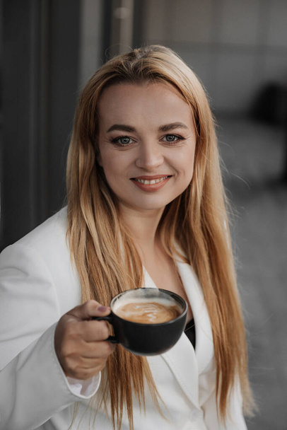 Blond stylová žena na nadměrné bílé sako pití aroma kávy a relaxovat na moderním městském pozadí - Fotografie, Obrázek