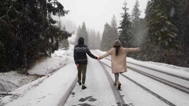 Νεαρό πολυεθνικό ζευγάρι σε ζεστά πουλόβερ χρονολογούνται στο χειμερινό δάσος στις διακοπές των Χριστουγέννων. Ευτυχισμένος χαρούμενος άντρας και γυναίκα απολαμβάνουν το πρώτο χιόνι στις διακοπές της Πρωτοχρονιάς. Εξωτερική δραστηριότητα, κρύος καιρός. Παραμονή Χριστουγέννων - Πλάνα, βίντεο