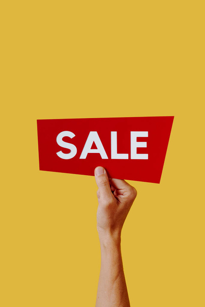 a man holds a red sign with the text sale, on a yellow background with some blank space on top - Foto, Imagen