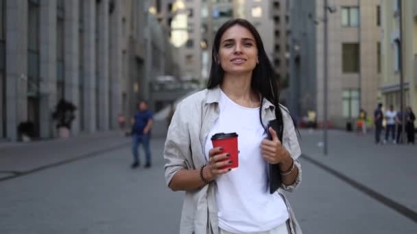 Successful young beautiful young woman with tablet and coffee cup walking between business buildings and smiling with joy. Attractive business girl. Career people. - Footage, Video