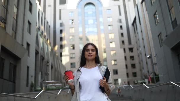 Successful young beautiful young woman with tablet and coffee cup walking between business buildings and smiling with joy. Attractive business girl. Career people. - Metraje, vídeo