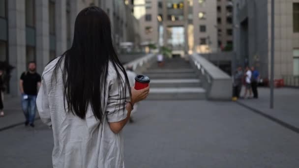 Succesvolle jonge mooie jonge vrouw met tablet en koffiebeker wandelen tussen zakelijke gebouwen en glimlachen van vreugde. Aantrekkelijk zakenmeisje. Beroepsmensen. - Video