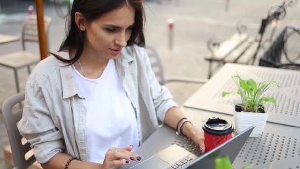 Freelancer nainen nauttii kahvia työskennellessään ulkona kannettavan tietokoneen kytketty julkiseen Wi-Fi. Tyylikäs opiskelija tyttö opiskelee verkossa kaupungissa. - Materiaali, video